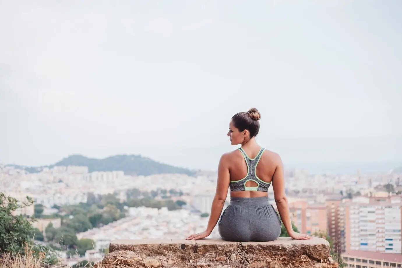 Женщина сидит на камне перед городом и смотрит в сторону.